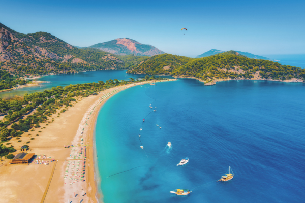 Aerial shot over the sea with a golden sandy beach on the left hand side and various mountain peaks in the background