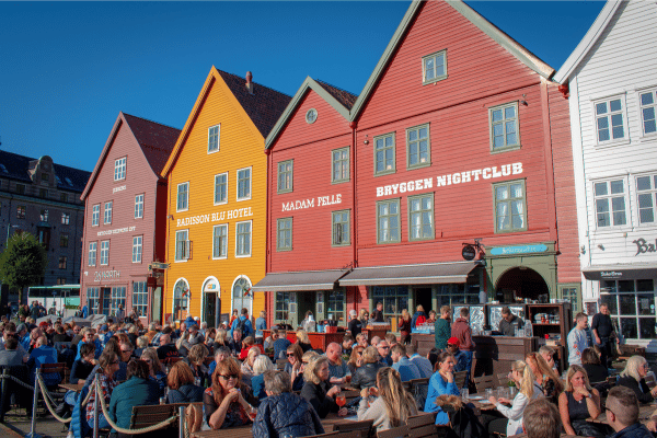 People eating and drinking on tables in front of the pointed wooden buildings of Bryggen