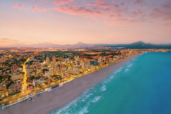 Alicante beach at sunset with the Mediterranean Sea on the right hand side of the beach and the city on the left hand side