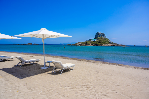 A beach with sun loungers looking out towards an island in the sea
