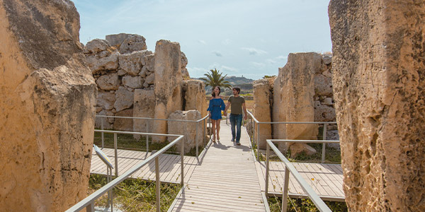 Two tourists walk between stones at Ġgantija Archaeological Park 