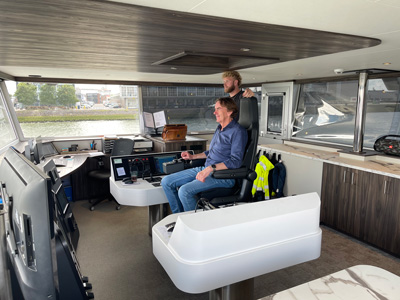 Ad Koppejan in de stuurhut op de stoel met bemanningslid ernaast