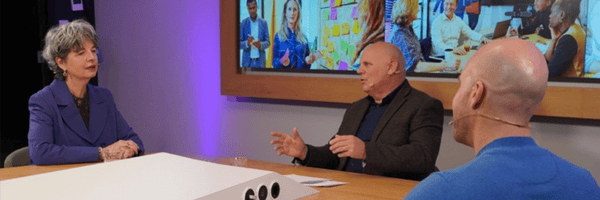 Een vrouw en twee mannen zitten aan tafel en zijn met elkaar in gesprek.