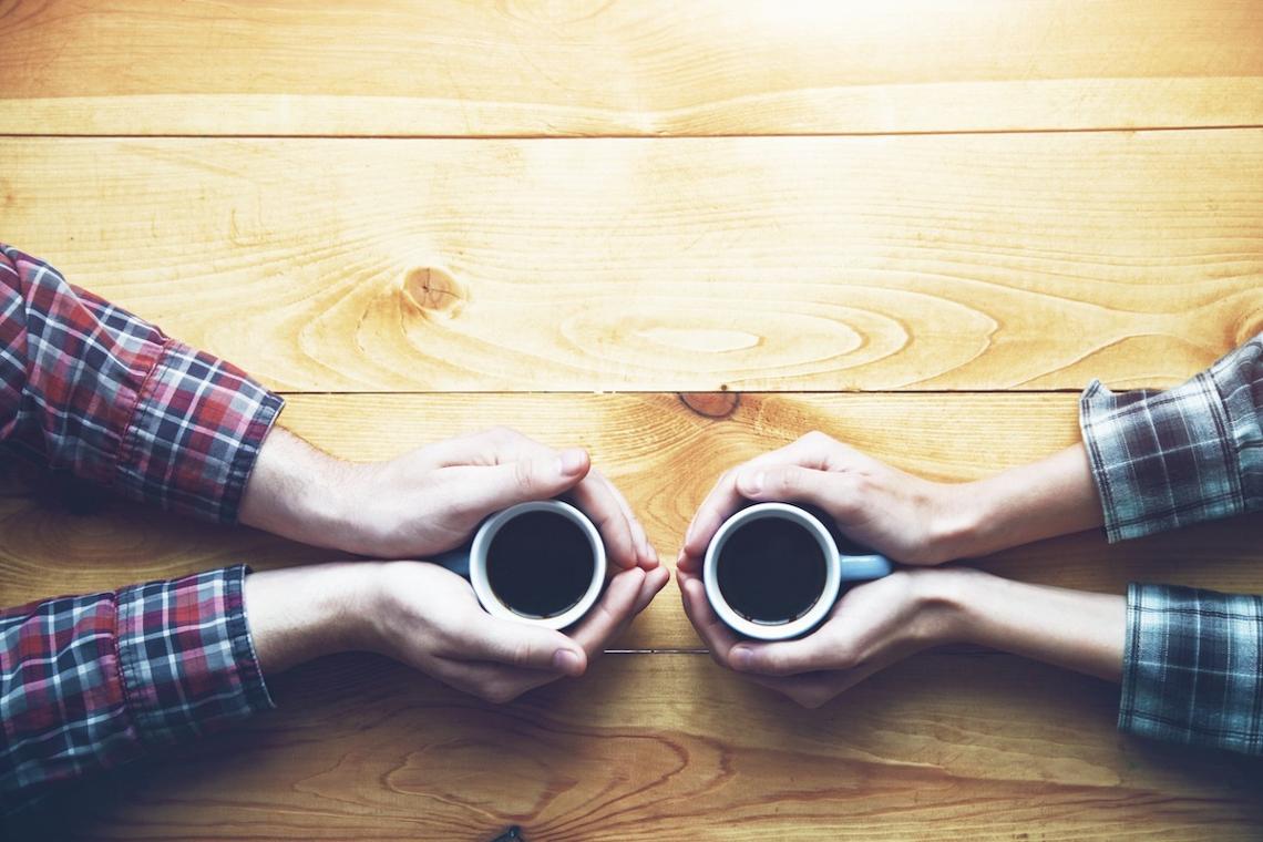 Foto van bovenaf van de handen van twee personen die een kop koffie vasthouden