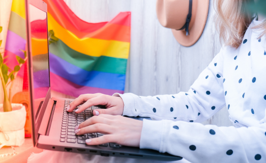 iemand achter een laptop met een regenboogvlaggetje op het bureau