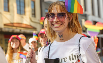 Een vrouw bij een Pride Walk kijkt lachend de camera in.