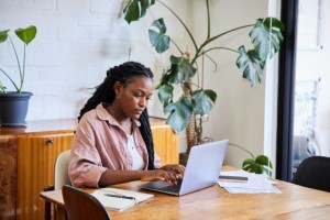 Een vrouw zit in een woonkamer aan een tafel met een laptop voor zich