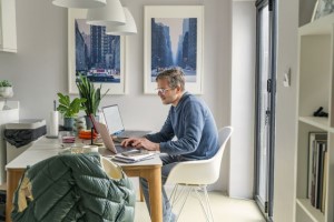 Een man zit aan een eettafel achter een laptop