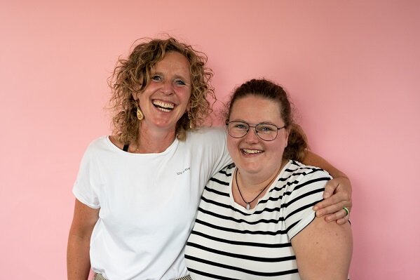 Lot en Lisa lachend op de foto met een roze achtergrond