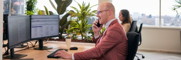Een man zit achter een bureau met daarop beeldschermen te bellen.
