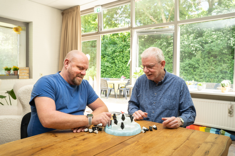 Begeleider zit samen met een cli&euml;nt aan een tafel een spelletje te spelen