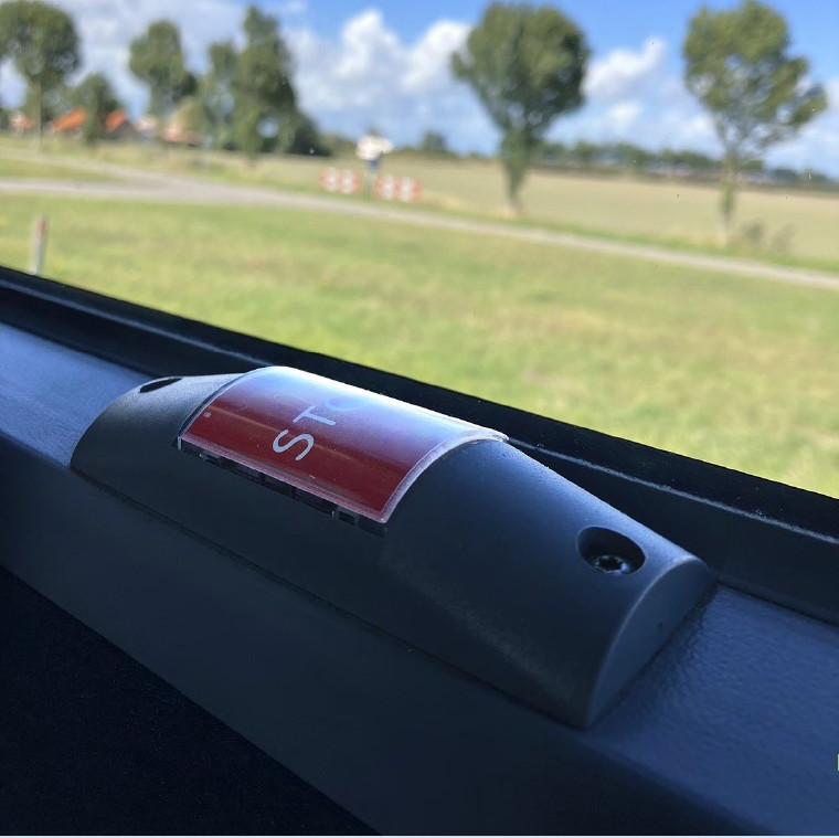 Een rode stopknop in een bus met op de achterrond Nederlands platteland