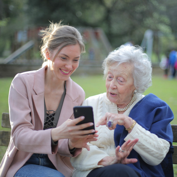 Een jongere en een oudere bekijken samen vrolijk een mobiele telefoon