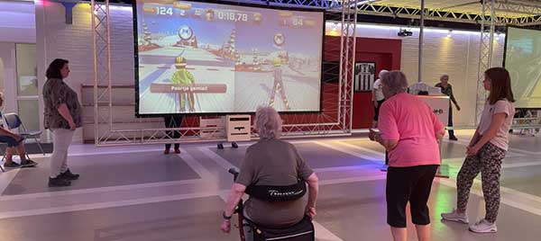 Oudere vrouw die gewichten optilt en daarbij wordt geholpen door een verzorgende