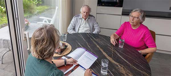 Oudere vrouw die gewichten optilt en daarbij wordt geholpen door een verzorgende