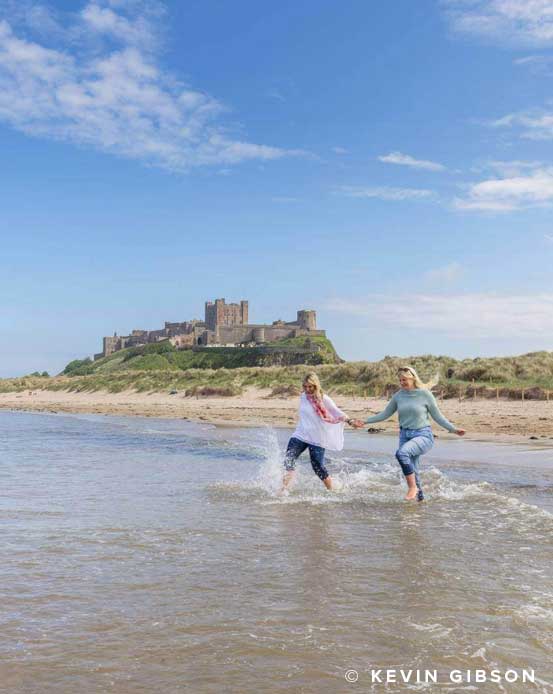 Two women running into the sea at Bamburgh