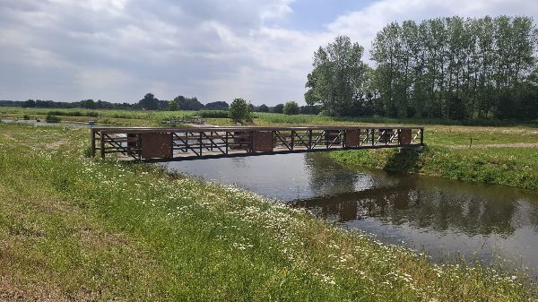 De wandelbrug met de zijpanelen met de afbeeldingen van de Romeinse grafvondsten. De brug ligt over de Essche Stroom. De kades zijn groen en bloemrijk