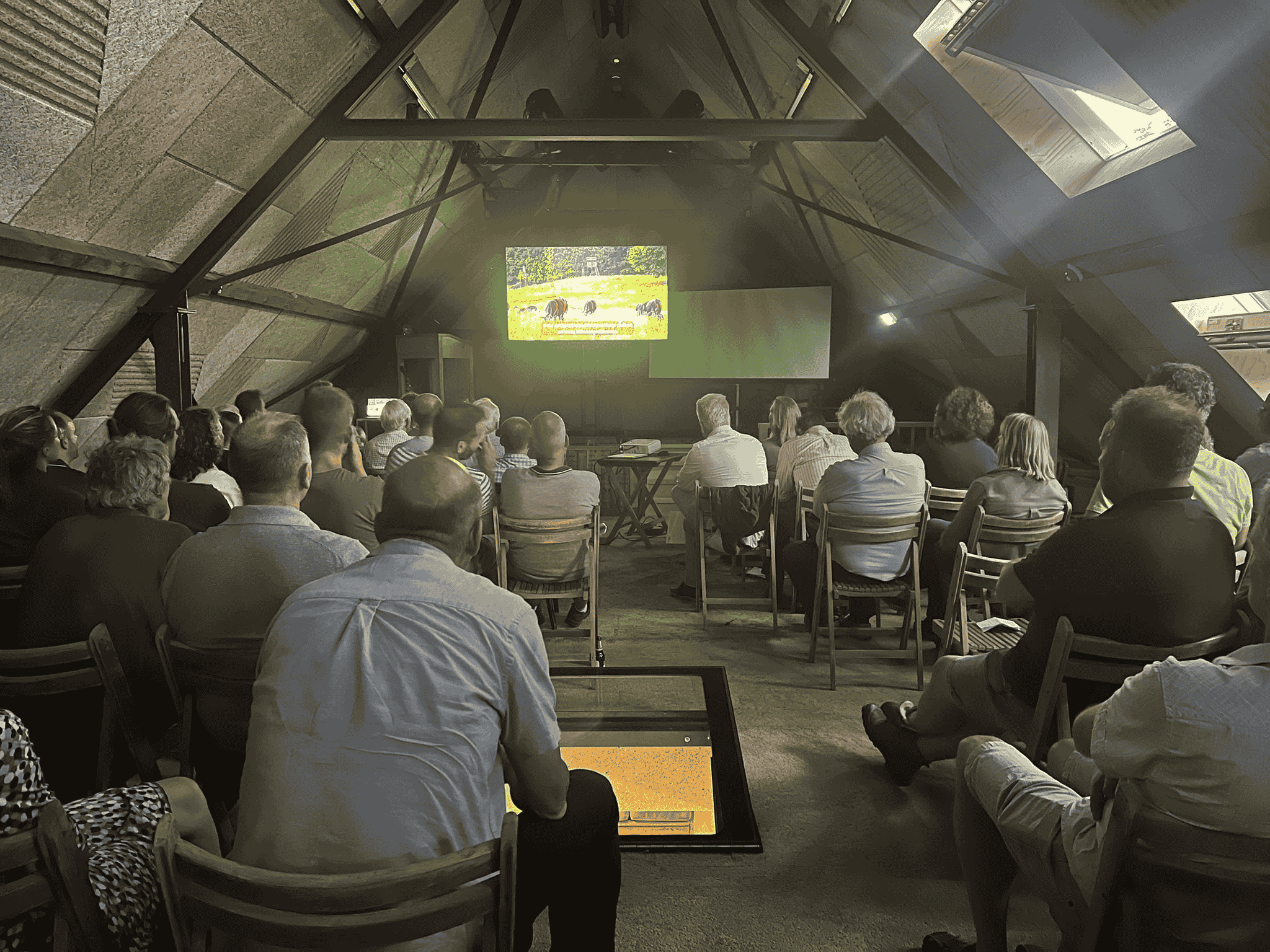 Mensen die naar de film  'ROOTS SO DEEP' kijken op groot scherm.