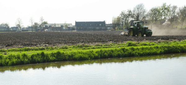 Een beek gegrenst aan een wei met zicht op een tractor