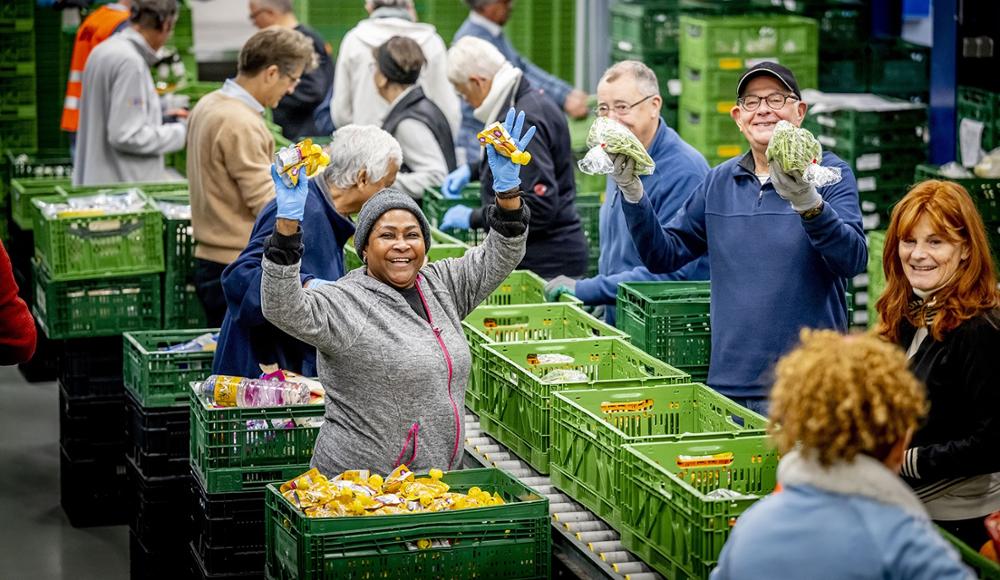 Lachende vrouw en man in een voedselbank met de handen in de lucht tijdens het inpakken van voedingsmiddelen 