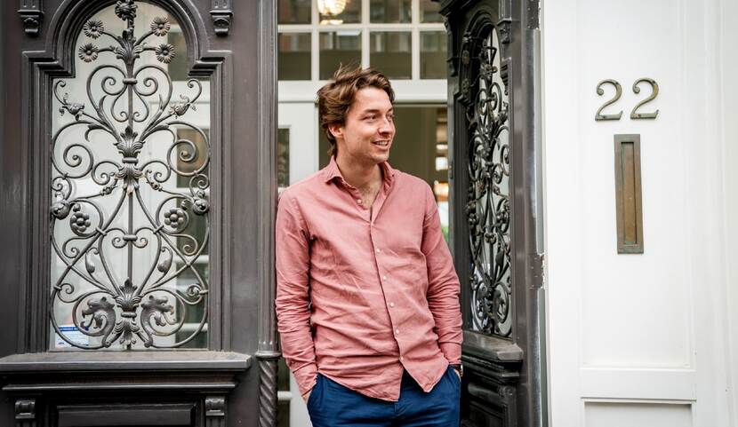 Jurriaan Parie van Algorithm Audit in de deuropening  van een pand. Hij draagt een roze overhemd en een blauwe broek.