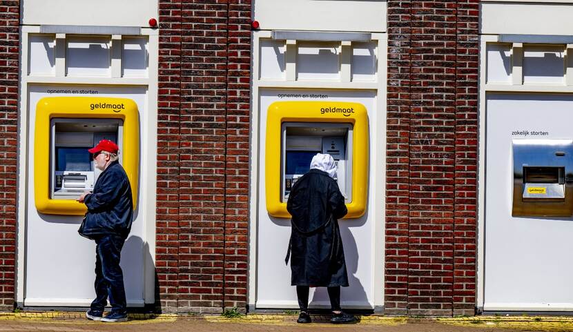 Drie pinautomaten en twee personen die aan het pinnen zijn