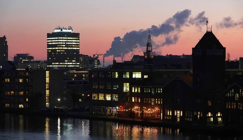 Zaandam in de schemering met op de achtergrond silhouetten van gebouwen en een pijp van een fabriek met vervuilend lucht