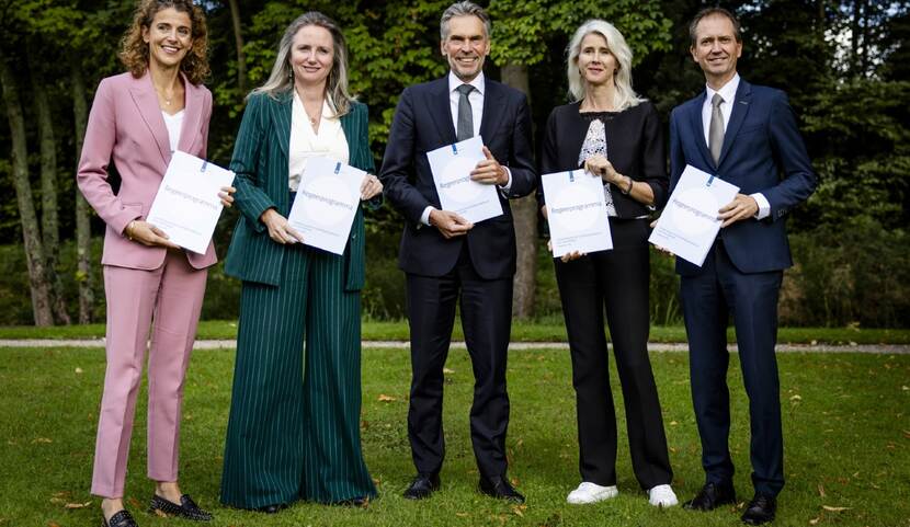 Sophie Hermans (VVD), Fleur Agema (PVV), minister-president Dick Schoof, Mona Keijzer (BBB) en Eddy van Hijum (NSC) die op een grasveld het regeerprogramma vasthouden.