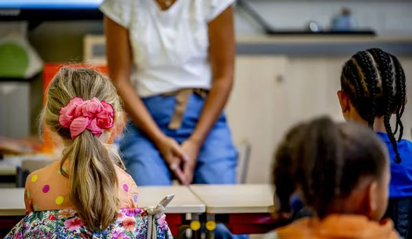Foto gemaakt in een klas op school. De kinderen zijn vanaf de achterkant te zien en op de voorgrond zie je de lerares. 