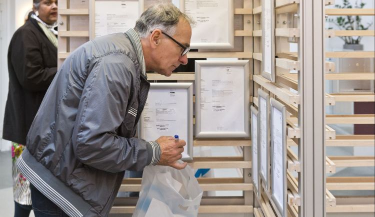 Een persoon met grijs haar en een bril die met een tas van het UWV mogelijk naar vacatures kijkt