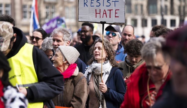 Deelnemers aan de landelijke demonstratie tegen discriminatie, racisme en fascisme verzamelen op de Dam. De protestmars werd door diverse organisaties georganiseerd in het kader van de internationale dag tegen racisme. Een vrouw houdt een bord omhoog met de tekst 'resist hate'.