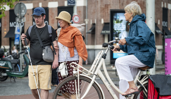 Drie personen in het straatbeeld, waarvan &eacute;&eacute;n persoon met visuele beperking