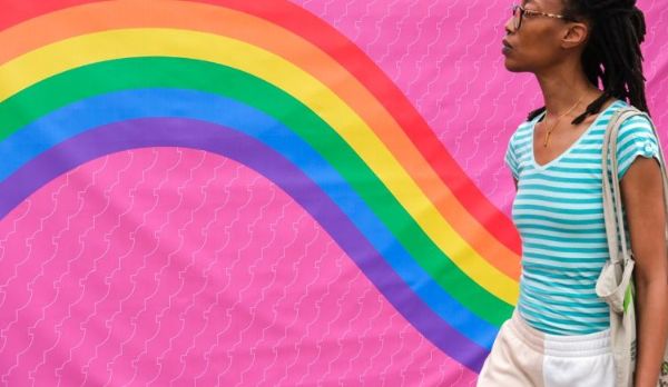 Een persoon voor een muur waarom een regenboog is geschilderd