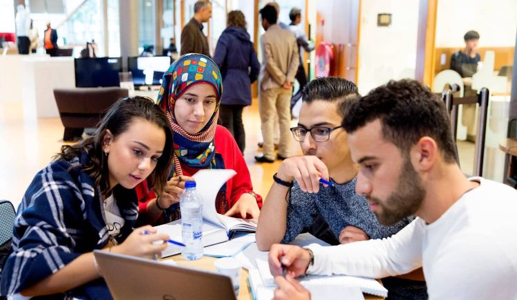 Groep van vier leerlingen op school aan tafel met boeken en een laptop