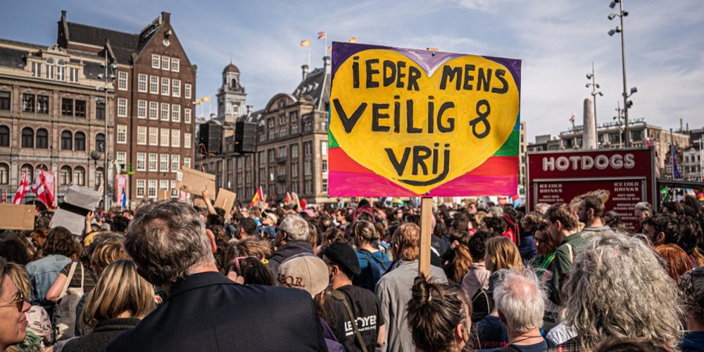 Personen op de Dam in Amsterdam tijdens een demonstratie tegen Racisme en Fascisme. Een protestbord is duidelijk zichtbaar met de tekst 'ieder mens veilig en vrij'.
