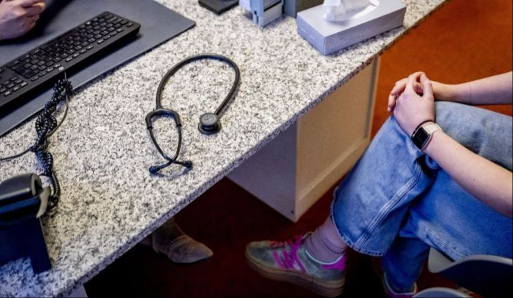 Stethoscoop op een bureau en een persoon achter het bureau waarvan alleen de voeten, benen en armen zijn te zien