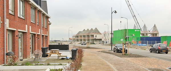 Foto van een straat met nieuwe woningen. Linsk zijn de woningen klaar. Rechts staan nog betonnen skeletten.