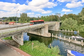 Een rode bus rijdt over een oud viaduct over de Ringvaart. 