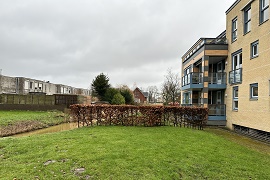 appartementen met aan de linkerzijde een grasveld, haag en een sloot.