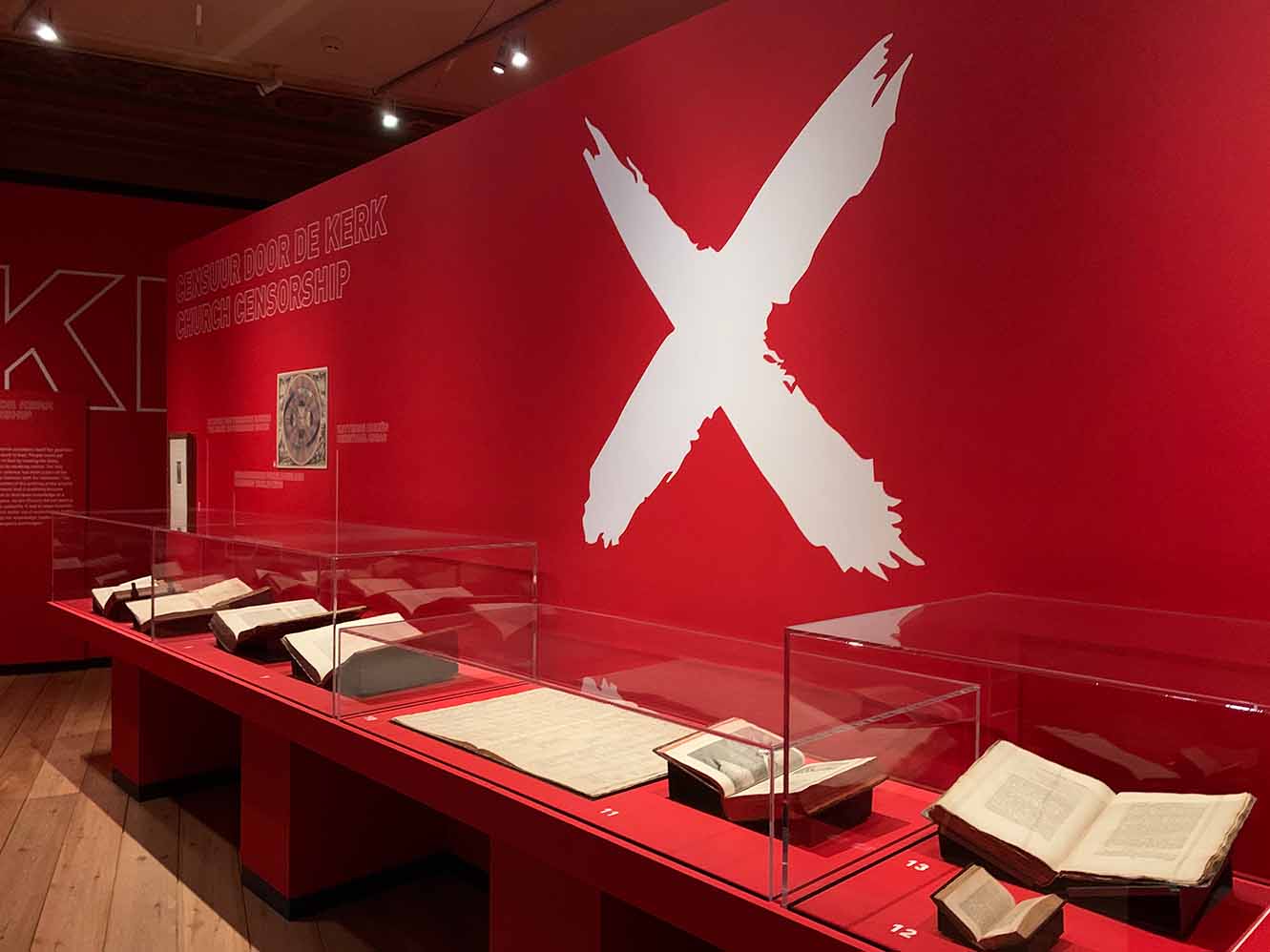 Scholier zit lachend in kleermakerszit in een bibliotheek en heeft een boek vast.