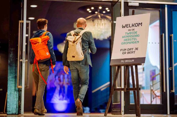 Mensen lopen naar binnen bij de ingang van Kennisdag Herstel Groningen