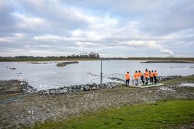 Mensen staan bij de uitgang van de getijdenduiker en kijken hoe het water binnenstroomt in het gebied achter de zeedijk.