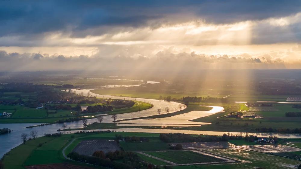De zon schijnt door de wolken op rivier de Maas