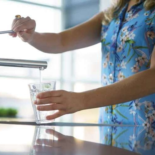 Vrouw vult glas water onder kraan