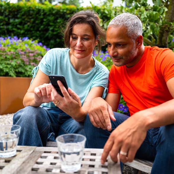 Man en vrouw in tuin kijken op telefoon