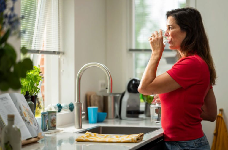 Vrouw drinkt water bij kraan in keuken