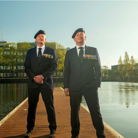 Twee veteranen in veteranentenue poseren op een steiger bij het water.