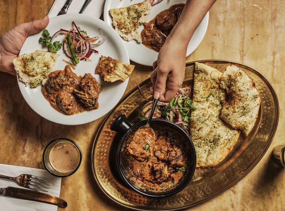 Two hands: one is dishing up a red/orange dish to someone holding a which plate