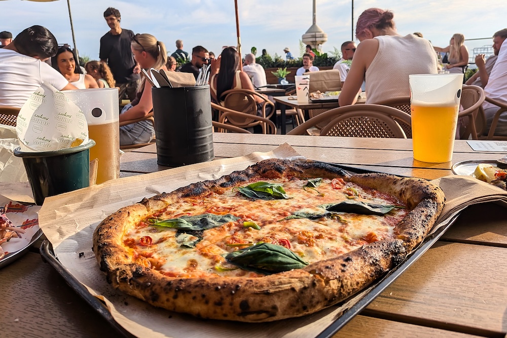 a pizza on the table and a couple of pints of beer. Lots of people in the background