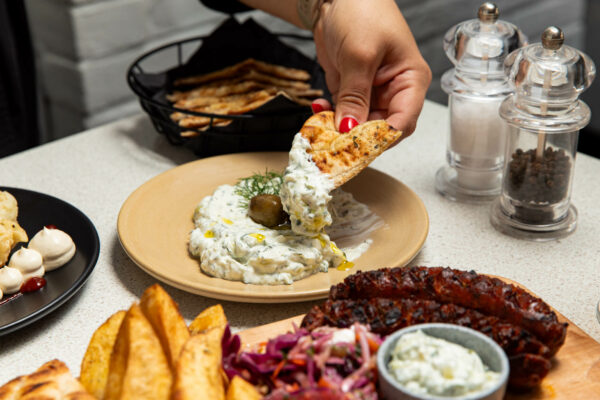 a hand with red nails scooping up a delicious looking yoghurty thing with some pitta bread